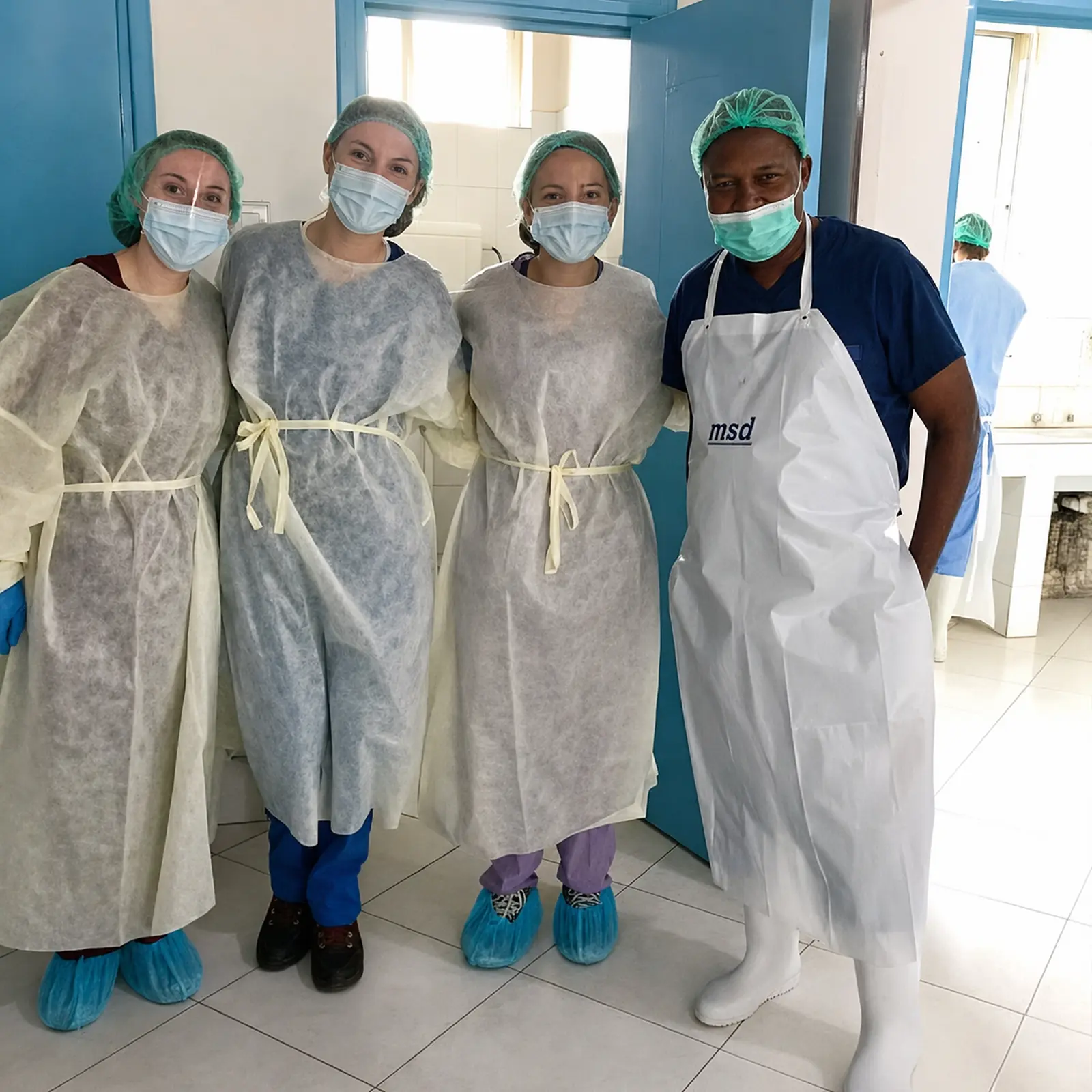 Nursing elective participants with a local healthcare professional wearing protective clothing in a Tanzanian clinical facility.